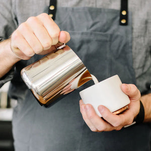 Barista pouring milk from a polished stainless steel pitcher, part of Espresso Accessories and Milk Pitcher, all about coffee.