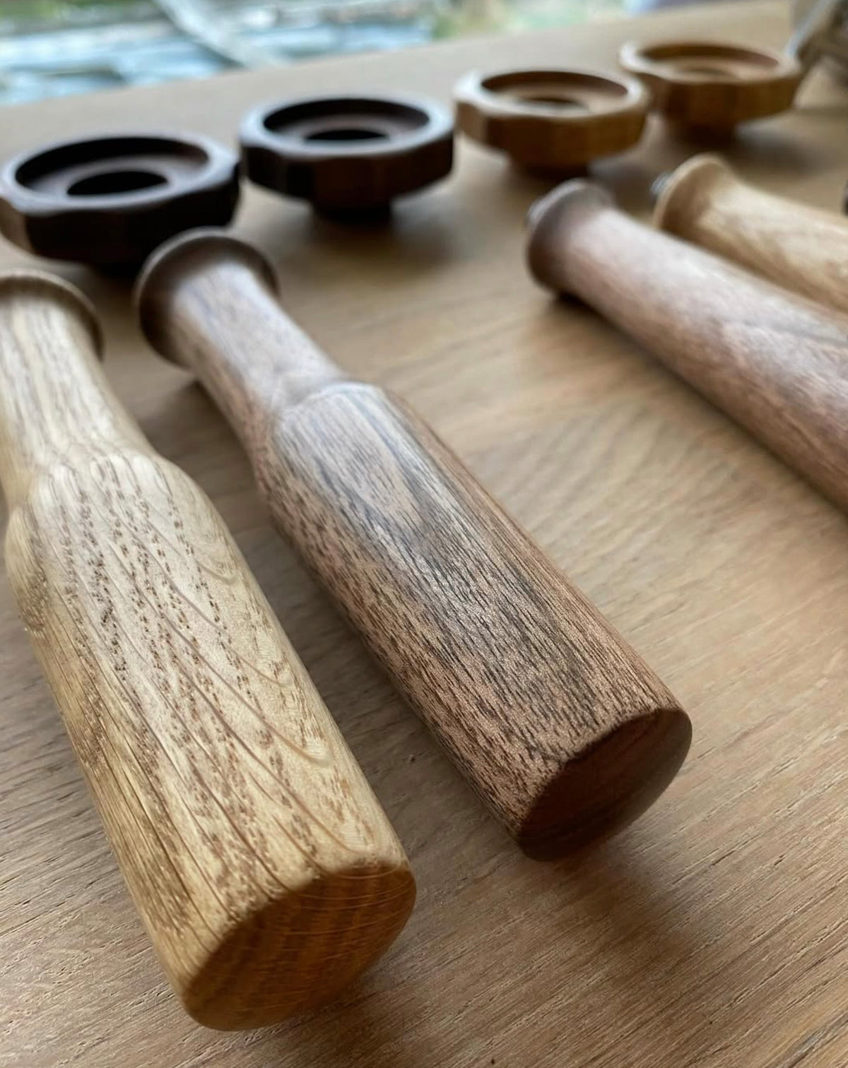 Handtag i trä för espressomaskiner placerade i rad på ett träbord i fokus framifrån.