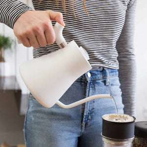 Hand pouring water from a white kettle with a narrow spout into a coffee filter, part of EspressoGear, all about coffee.