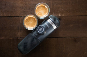 Portable espresso machine with two cups of espresso on a wooden surface, from portable coffee makers and barista equipment