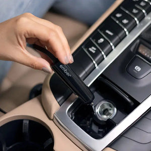Hand connecting car charger for Ember electric mug into car cigarette lighter for convenient charging.